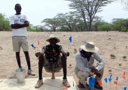Francis and John watch over yemane carefully as he places flags on several pieces of a broken pot.